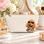 Cream makeup pouch with an apricot Poodle in sunglasses and a striped top on a vanity beside flowers