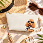Cream makeup pouch with an apricot Poodle in sunglasses and a striped top beside a straw hat and sunglasses